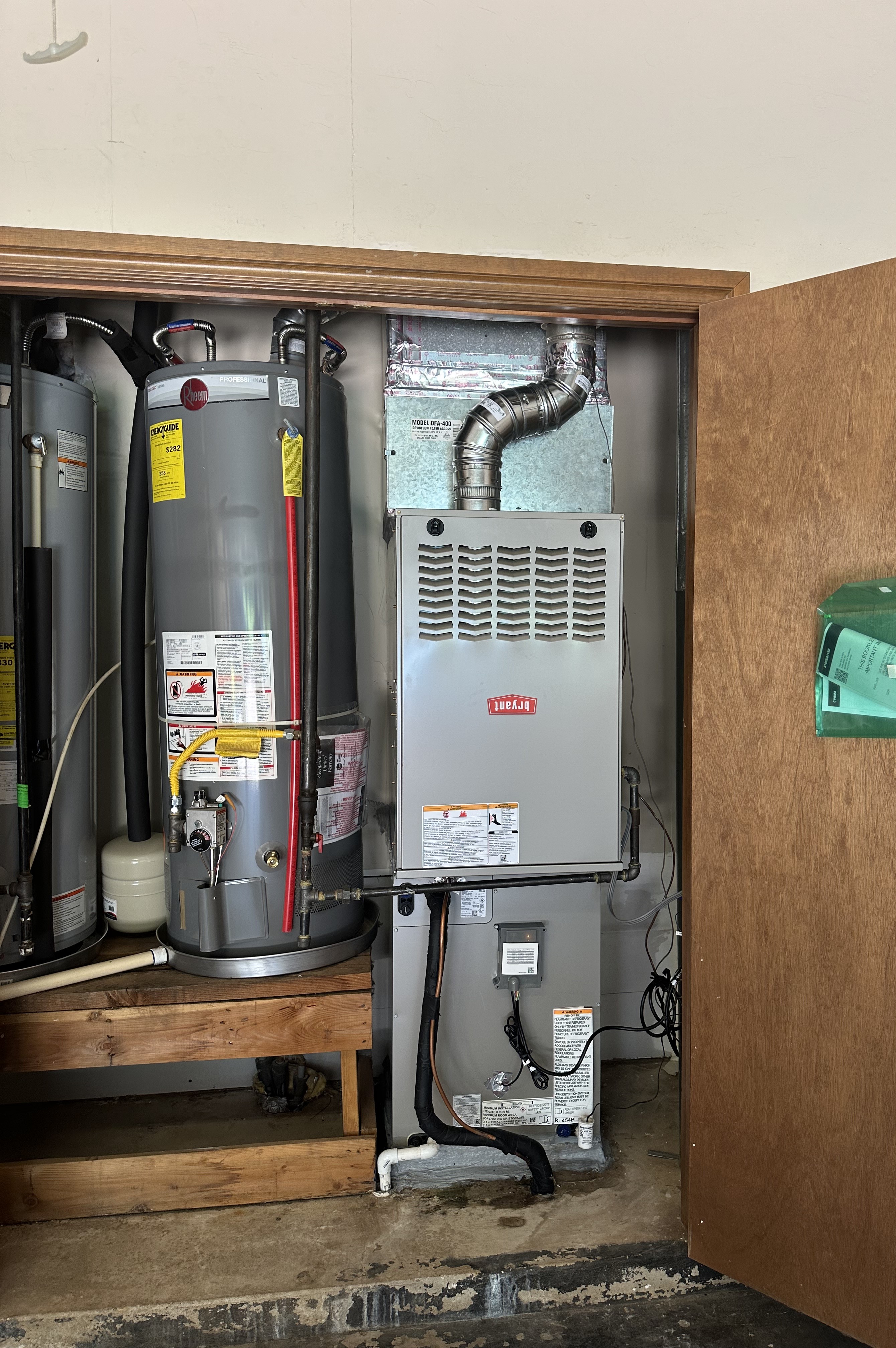 HVAC technician using a manifold gauge to check refrigerant levels on an outdoor air conditioning unit with exposed wiring and components.